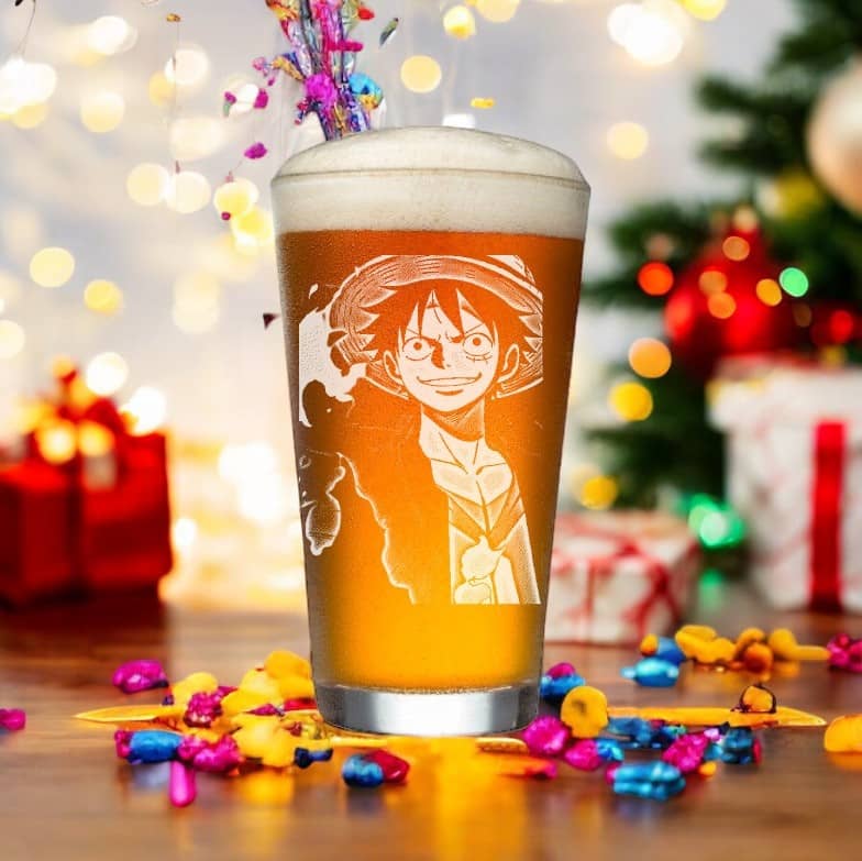 A Customized Anime Pint Glass from My Store is displayed on a table, featuring a unique etching of a cartoon character in a straw hat. This etched Manga Beer Mug makes it an ideal Anime Christmas Gift for Otaku collectors. In the background, vibrant lights and wrapped presents set the scene, with bright candies sprinkled around to enhance the cheerful atmosphere.