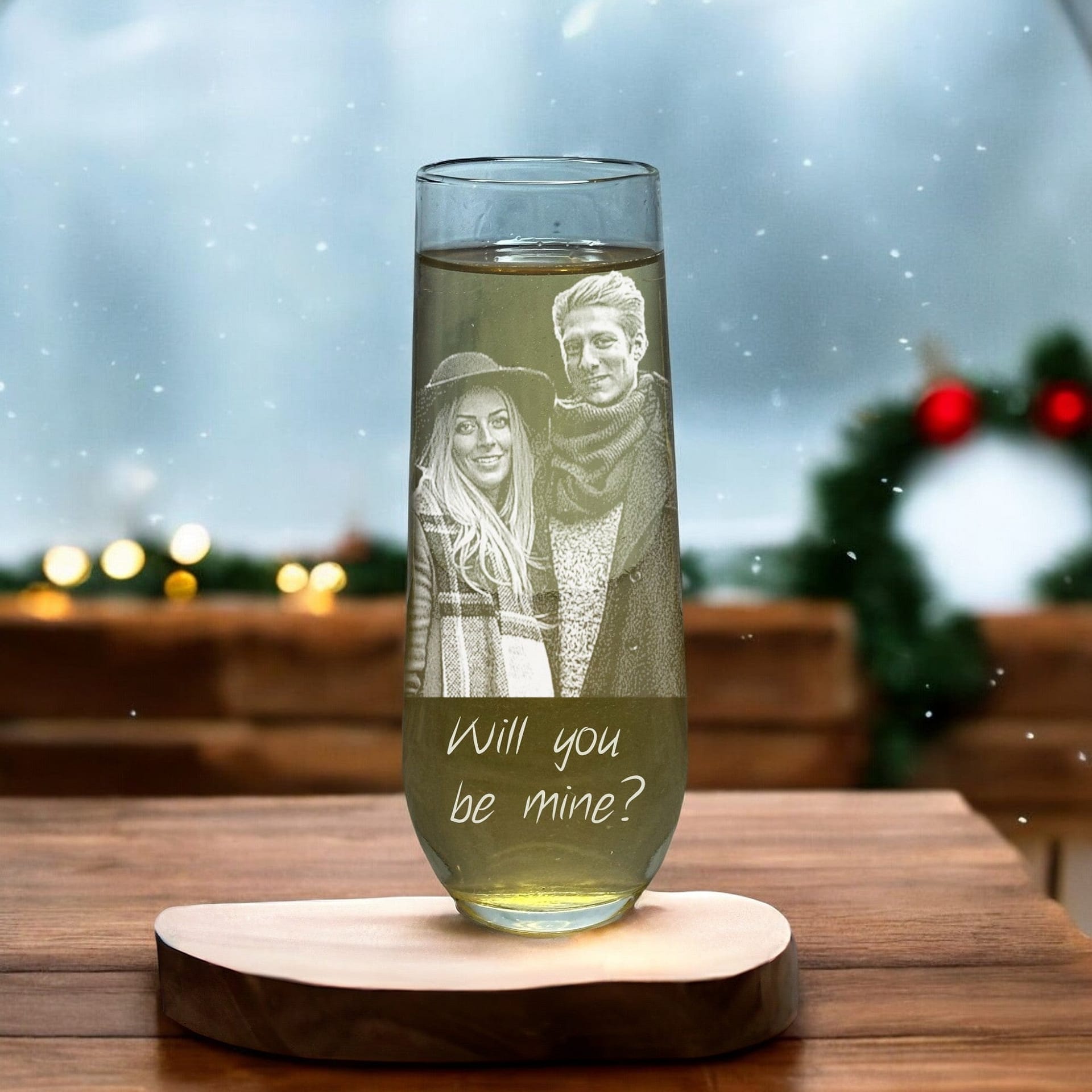 A customized stemless champagne flute from My Store, featuring an engraved photo of a couple along with the text "Will you be mine?" set against a warmly lit backdrop adorned with Christmas decorations like a wreath and twinkling lights, creating an ideal festive ambiance—perfect for thoughtful Christmas gifts.