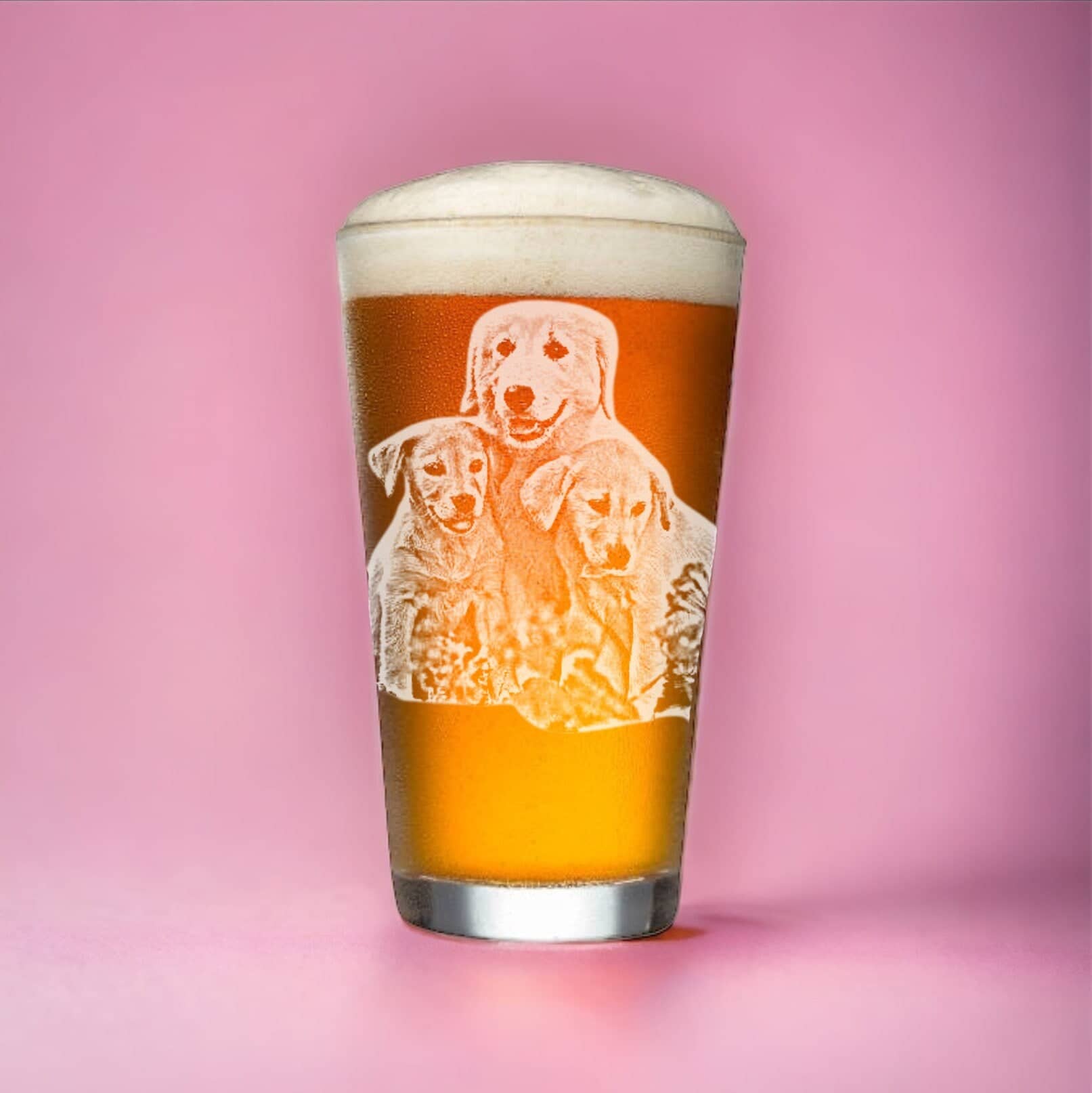 A pint glass filled with amber beer is set against a pink background, featuring the etched image of three Labrador puppies sitting together. This Personalized Pet Portrait Beer Glass from My Store showcases a frothy head on top, making it a charming and unique Dog Mom Christmas Gift.